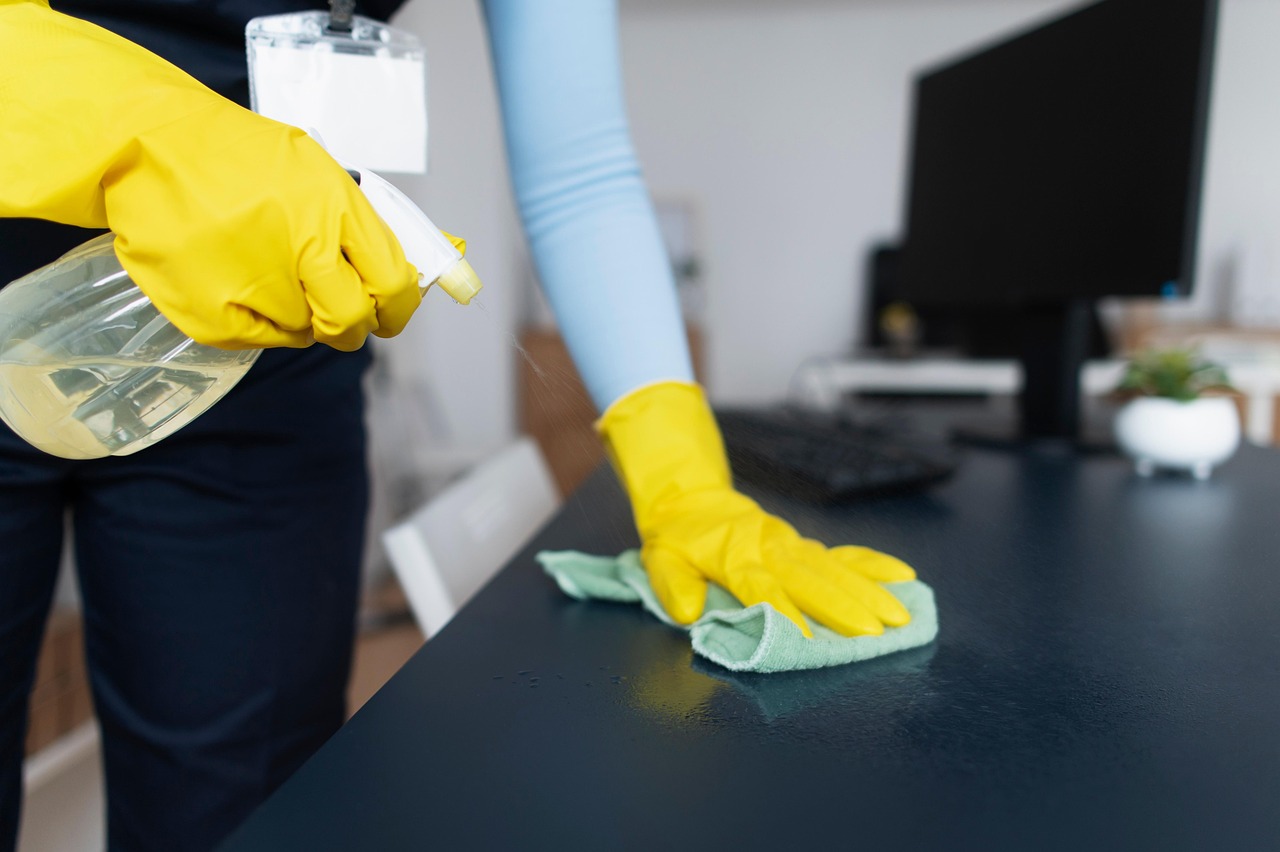 Reinigung einer Tischoberfläche mit Reinigungstuch und Schutzhandschuhen