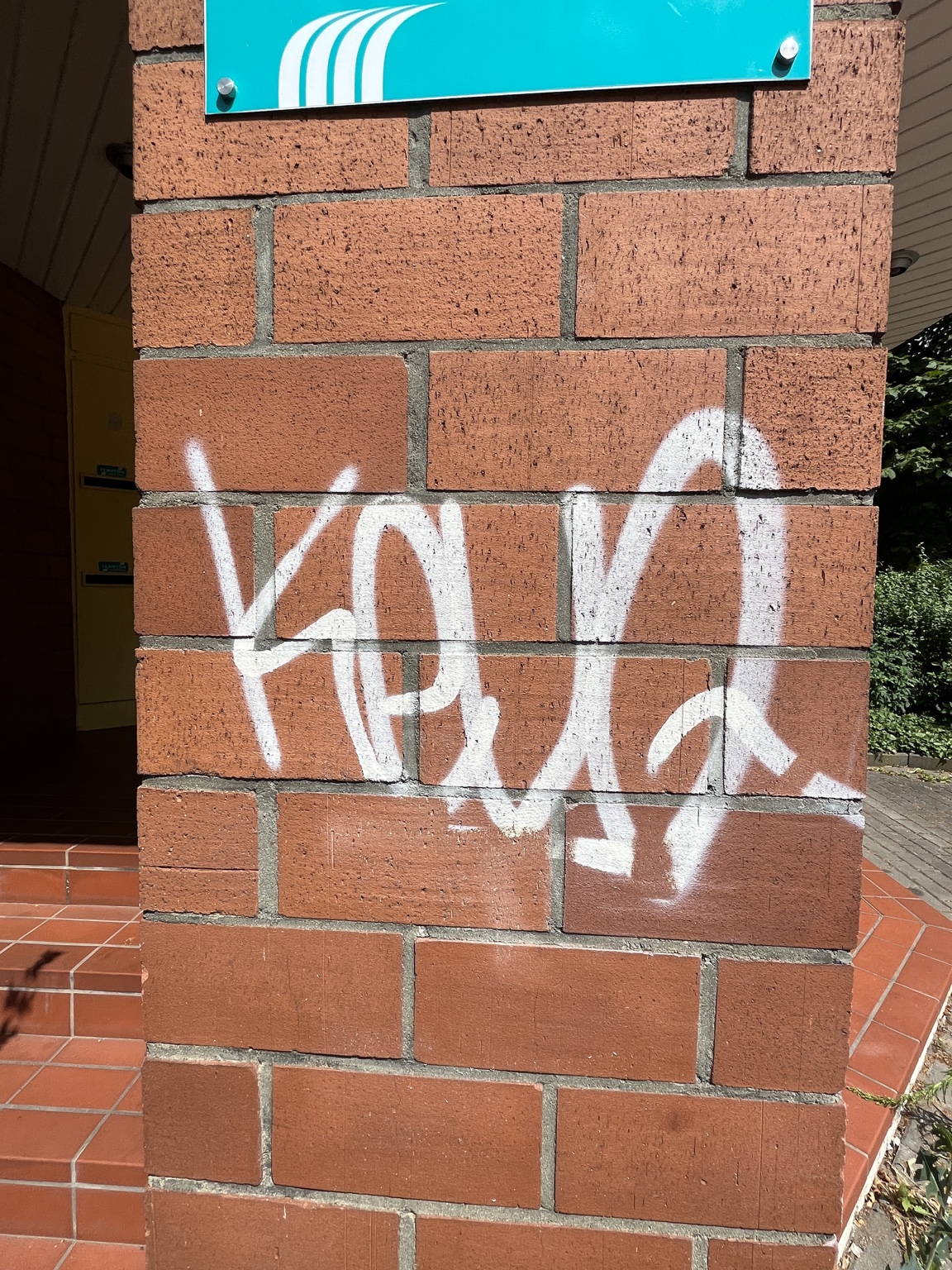 Weißer Graffiti-Schriftzug auf einer roten Klinkerwand